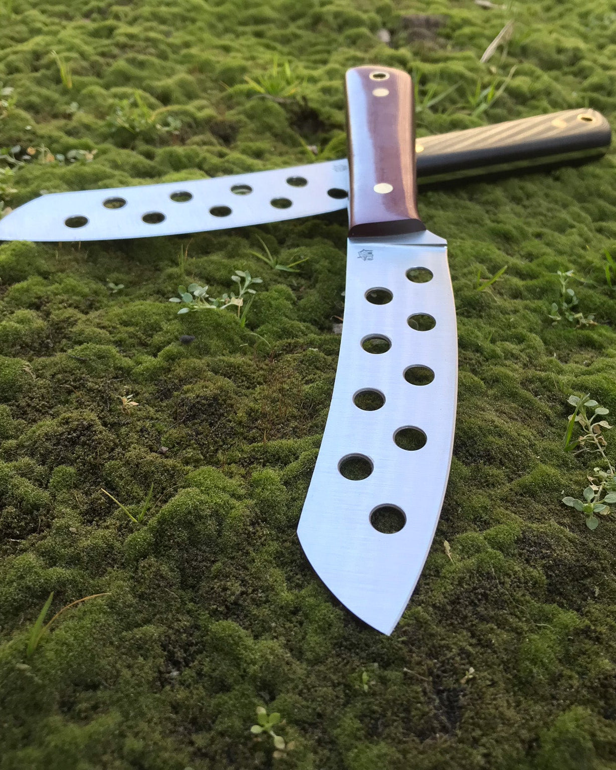 Two large knives with perforated blades on a grassy surface